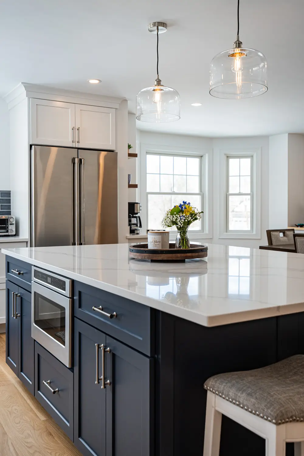 Modern kitchen with navy blue cabinetry, stainless steel appliances, quartz countertop, and decorative pendant lighting, featuring a vase of flowers on a wooden tray.
