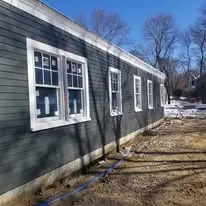 Newly installed gray siding on a residential building with white window trim, showcasing craftsmanship and renovation work by Clarke Building Company in West Newbury, MA.