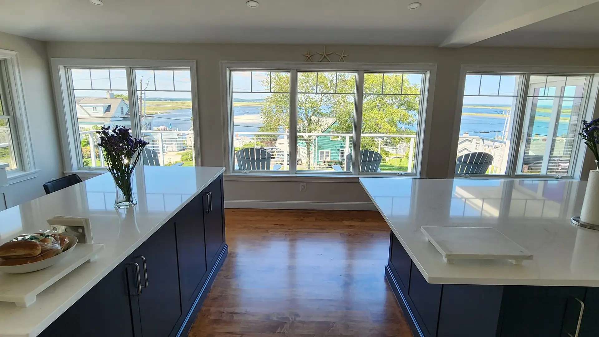Modern kitchen with dual islands, ocean view through large windows, and fresh flowers on the countertop, highlighting Clarke Building Company's custom renovation expertise.