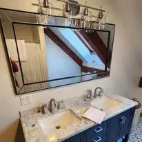Modern bathroom vanity with double sinks, stylish mirror, and light fixture.